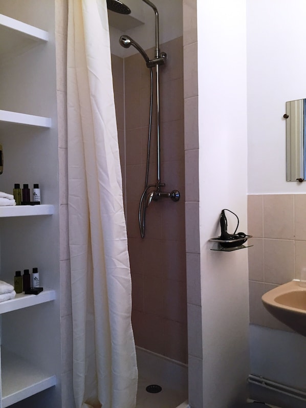 Un baño con ducha, lavamanos y repisas con artículos de aseo.