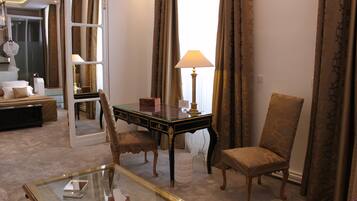 A hotel room with a glass coffee table, a desk with a lamp, a chair, a sofa, and a large mirror.