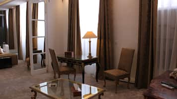 Una habitación de hotel con una mesita de vidrio, dos sillones, un escritorio con lámpara, un espejo y una cama.