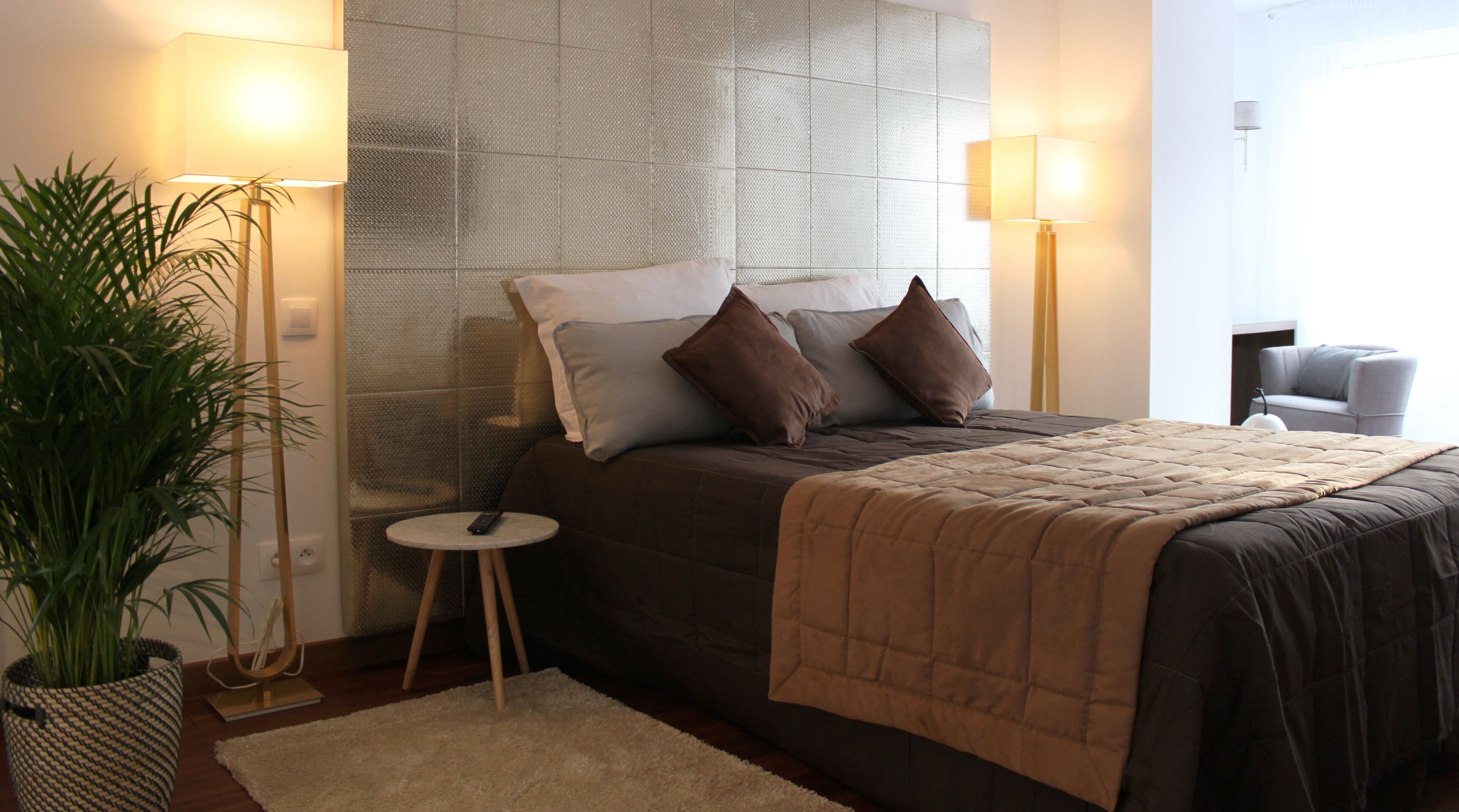 Un dormitorio moderno con una cama grande, dos lámparas de noche, una mesita redonda y una planta en maceta.