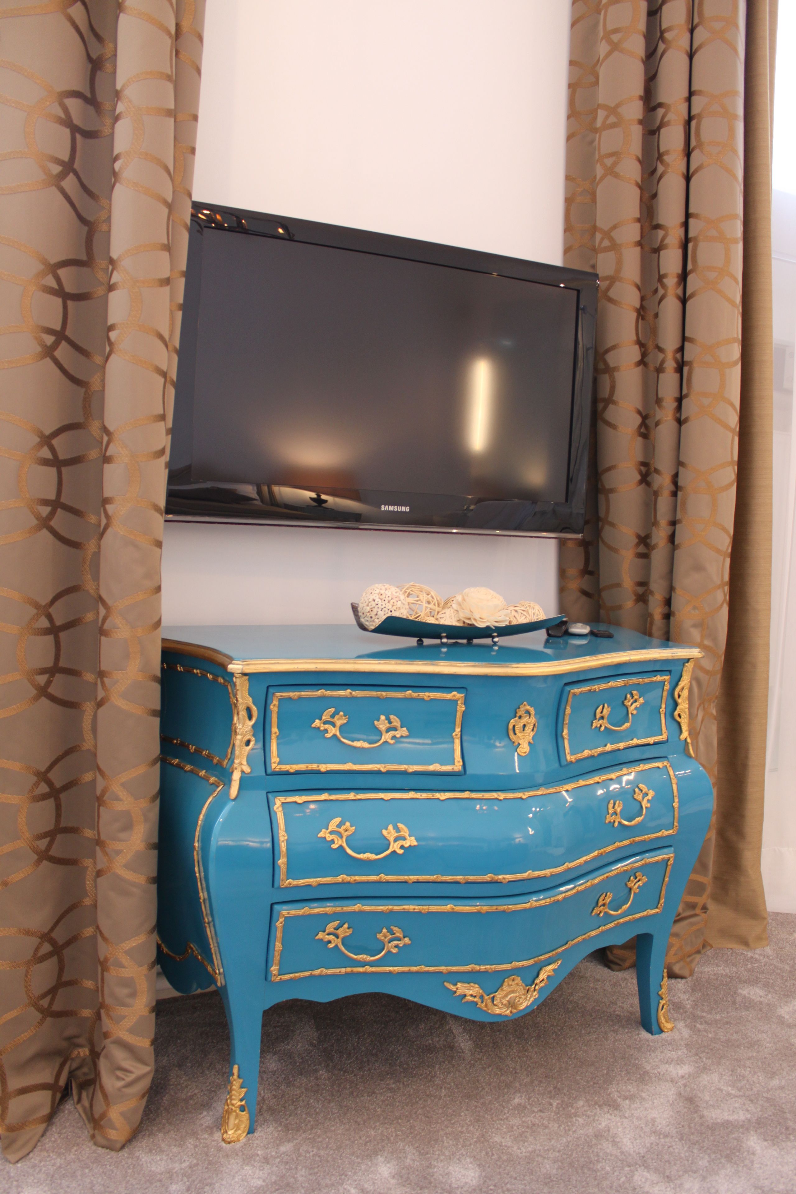 A blue dresser with gold trim and a television above it.