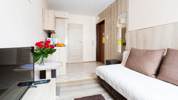 A modern hotel room with a bed, a desk with a vase of flowers, a mirror, and a wardrobe. - Aparthouse Apartamenty (Katowice)