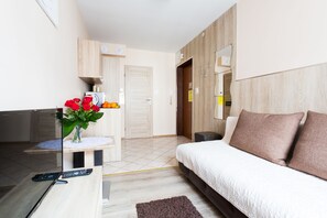 A modern hotel room with a bed, a desk with a vase of flowers, a mirror, and a wardrobe. - Aparthouse Apartamenty (Katowice)