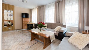 A modern living room with a wooden coffee table, beige sofa, and a television on a wooden cabinet. - Aparthouse Apartamenty (Katowice)