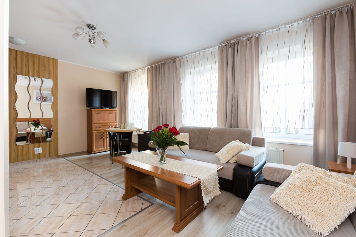 Una sala de estar moderna con una mesa de centro de madera, sofá color beige y un televisor sobre un mueble de madera.