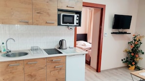 A compact kitchen with a microwave, sink, and kettle, a small white refrigerator, wooden cabinets, and a TV mounted on the wall. - Aparthouse Apartamenty (Katowice)