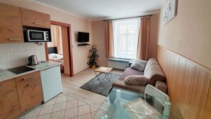 A compact living space with a kitchenette, a sofa, a glass table, and a television. - Aparthouse Apartamenty (Katowice)