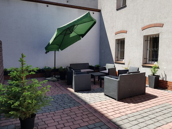 A patio with wicker furniture, a green umbrella, and potted plants. - Aparthouse Apartamenty (Katowice)