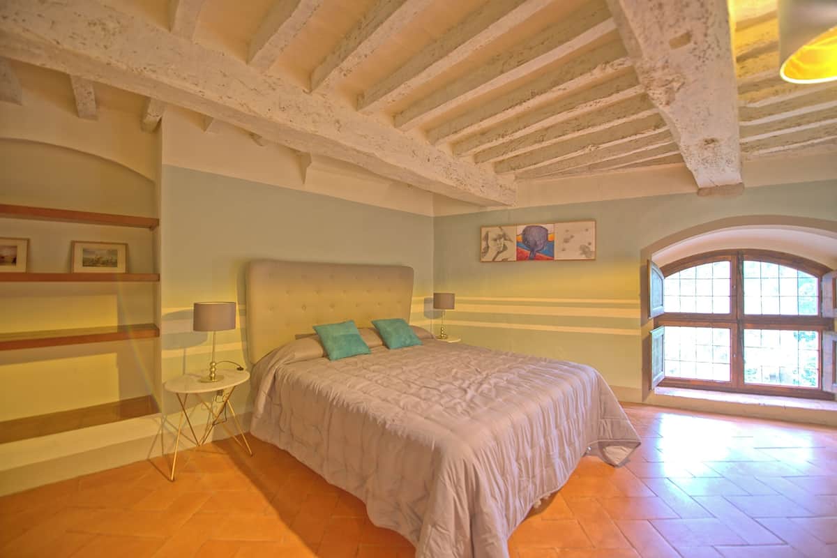 Quarto com cama grande, mesa de cabeceira pequena, luminária e janela com vista.