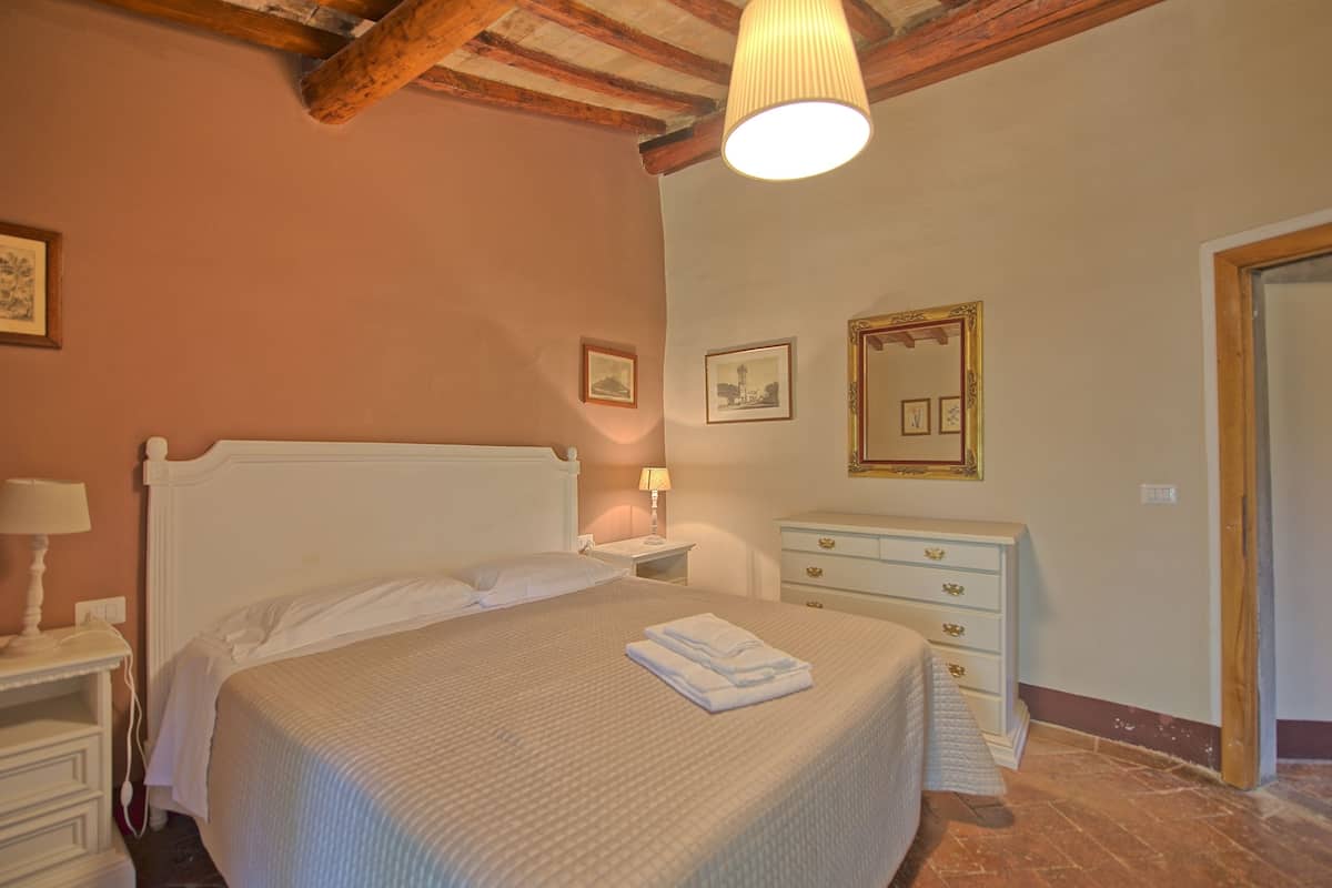 Quarto com cama, mesas de cabeceira, penteadeira e espelho.