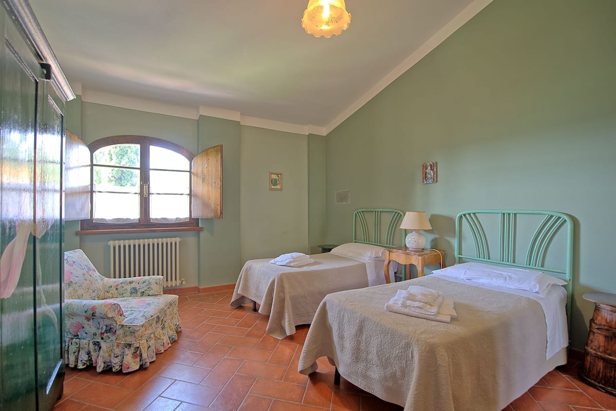 Quarto com duas camas, uma cadeira, uma janela e um radiador.