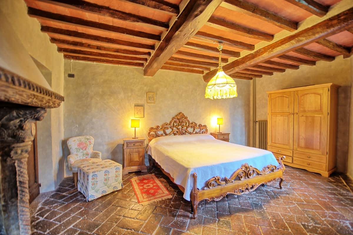 Quarto com cama de madeira, duas mesas de cabeceira, uma cadeira e um guarda-roupa.
