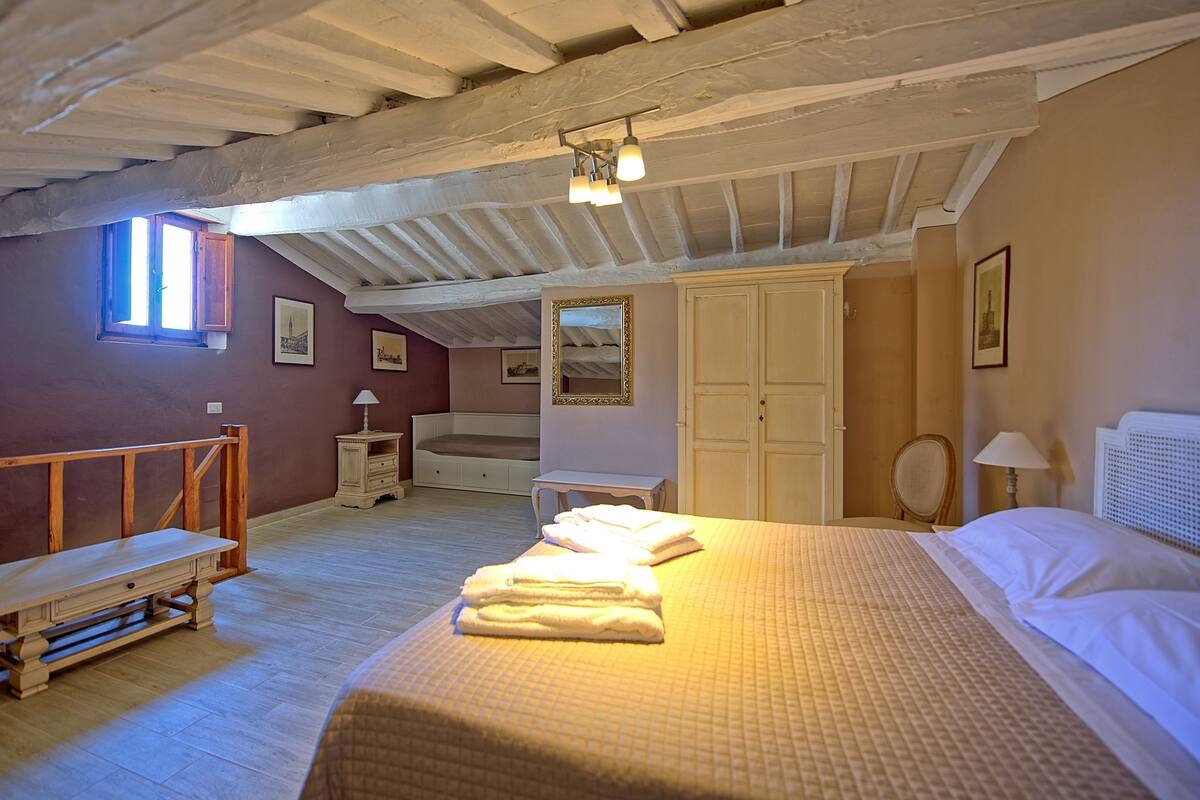 Quarto com cama, escrivaninha, cadeira e janela.