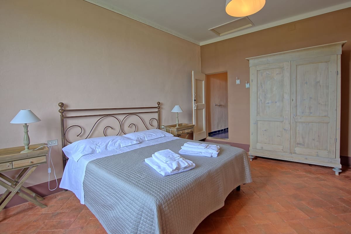 Quarto com cama, duas mesas de cabeceira com abajures, guarda-roupa e espelho.