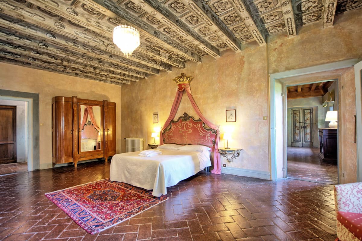 Quarto com uma cama grande, teto ornamentado e dossel vermelho.