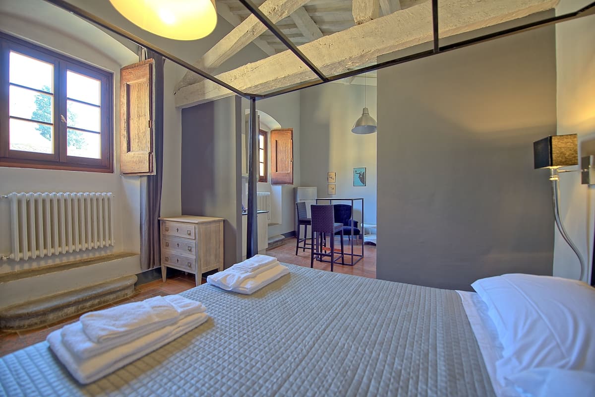 Quarto com uma cama grande, cômoda de madeira, escrivaninha e cadeira, além de vista para o exterior.