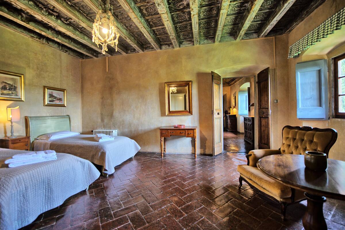 Quarto com duas camas, uma mesa de madeira, uma cadeira, um espelho e um candelabro.