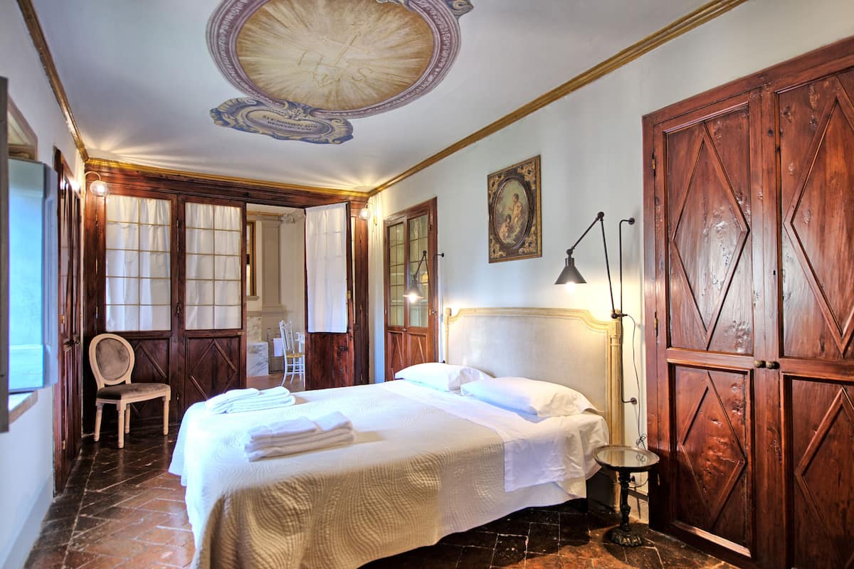 Quarto de hotel com uma cama grande, armário de madeira e um candelabro.