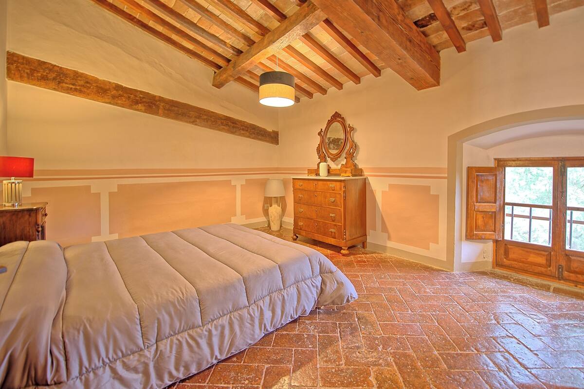 Quarto com cama grande, vigas de madeira, penteadeira e espelho.