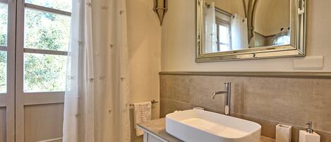 A bathroom with a large mirror, a sink, and a window with curtains.