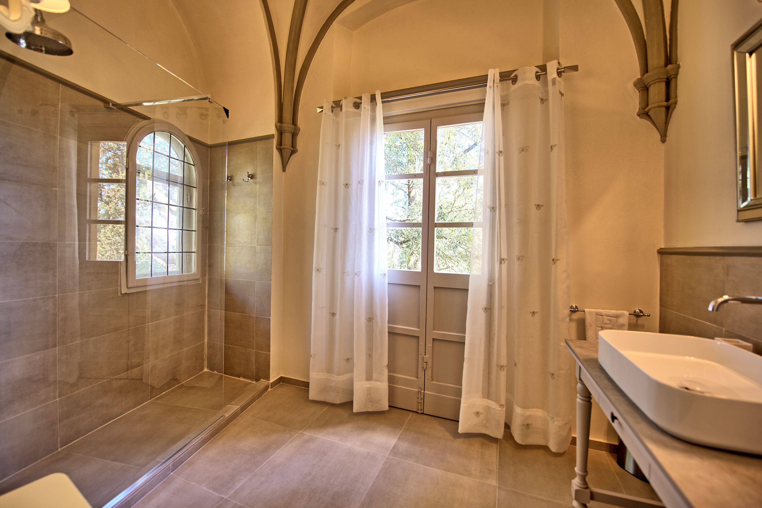 Un baño con ducha, lavamanos y ventana con cortinas.