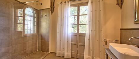 Un baño con ducha, lavamanos y ventana con cortinas.