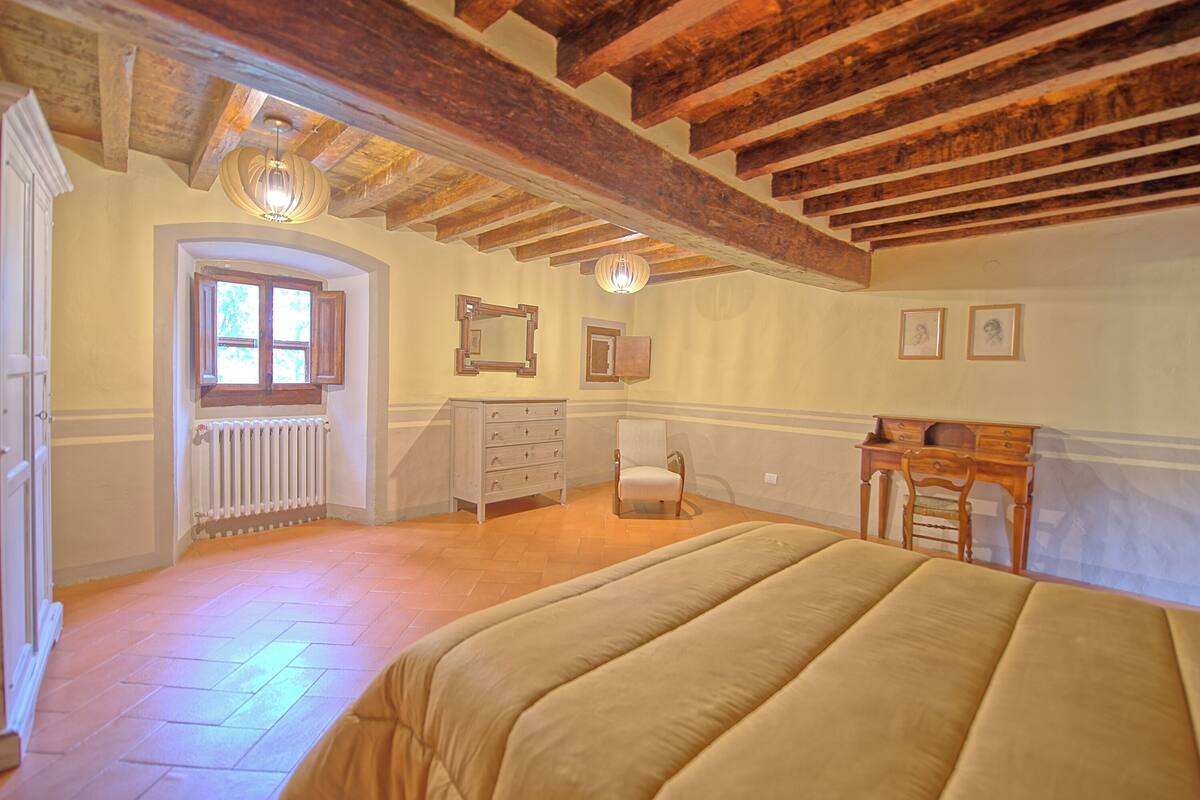 Um quarto com teto de madeira, uma cama, cômoda, cadeira e escrivaninha.