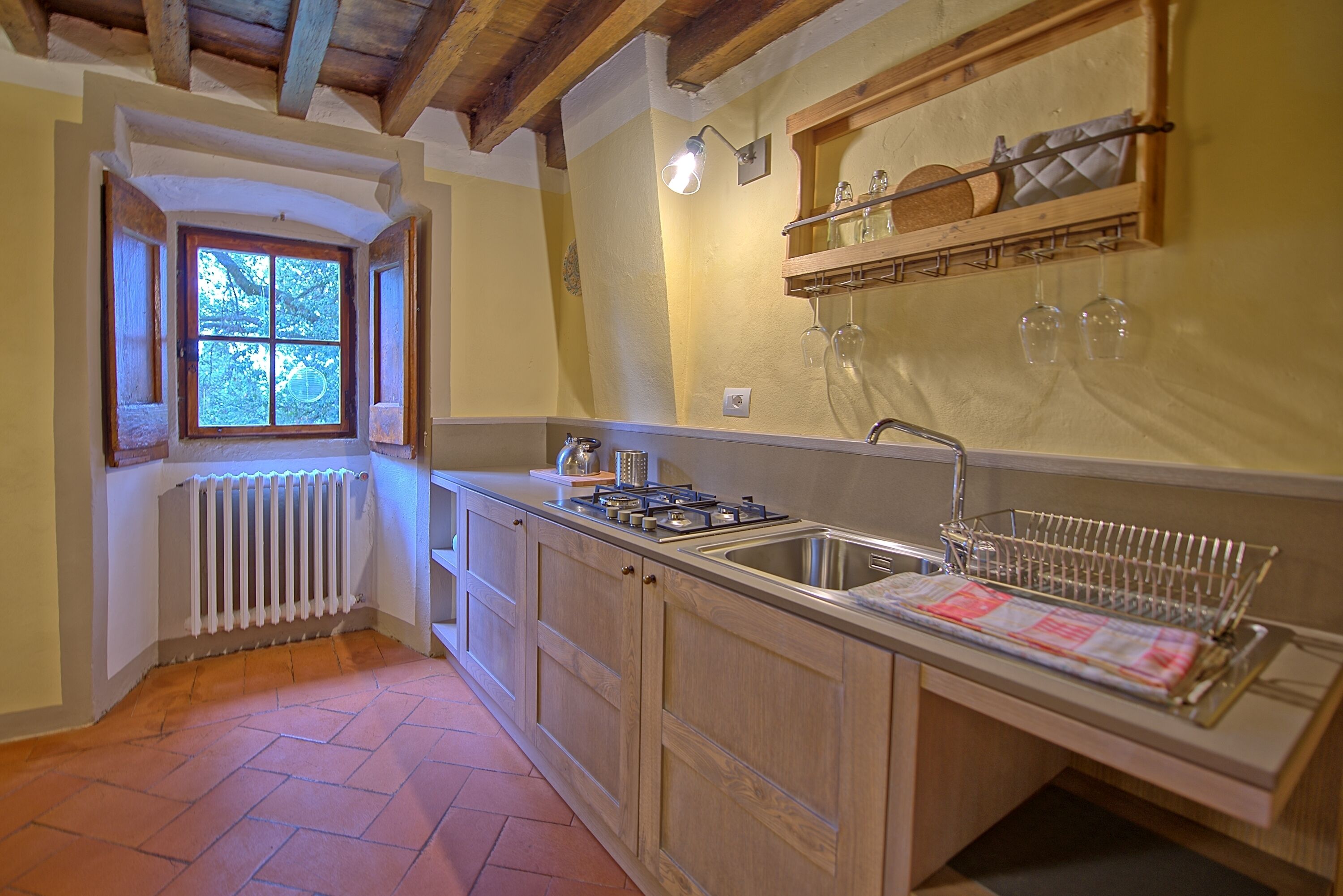 A kitchen with wooden cabinets, a built-in stove, a sink, and a window with a view of trees.