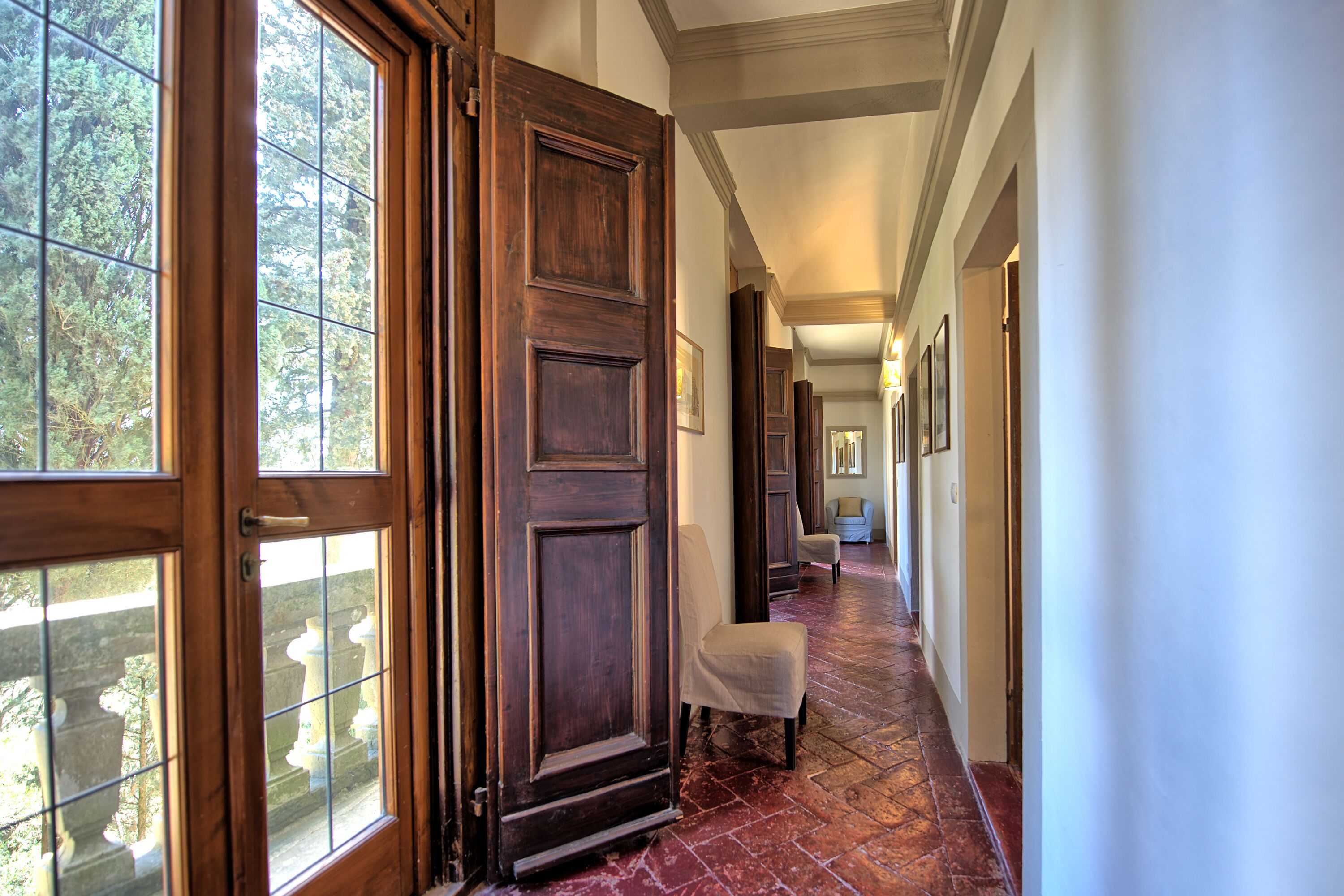 A hallway with a wooden door, a chair, and a view of trees through the door.
