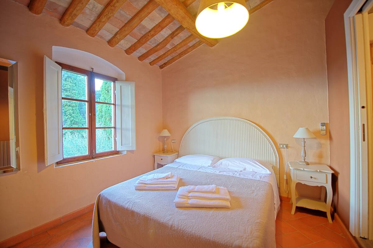 Quarto com cama, duas mesas de cabeceira, janela e luminária de teto.