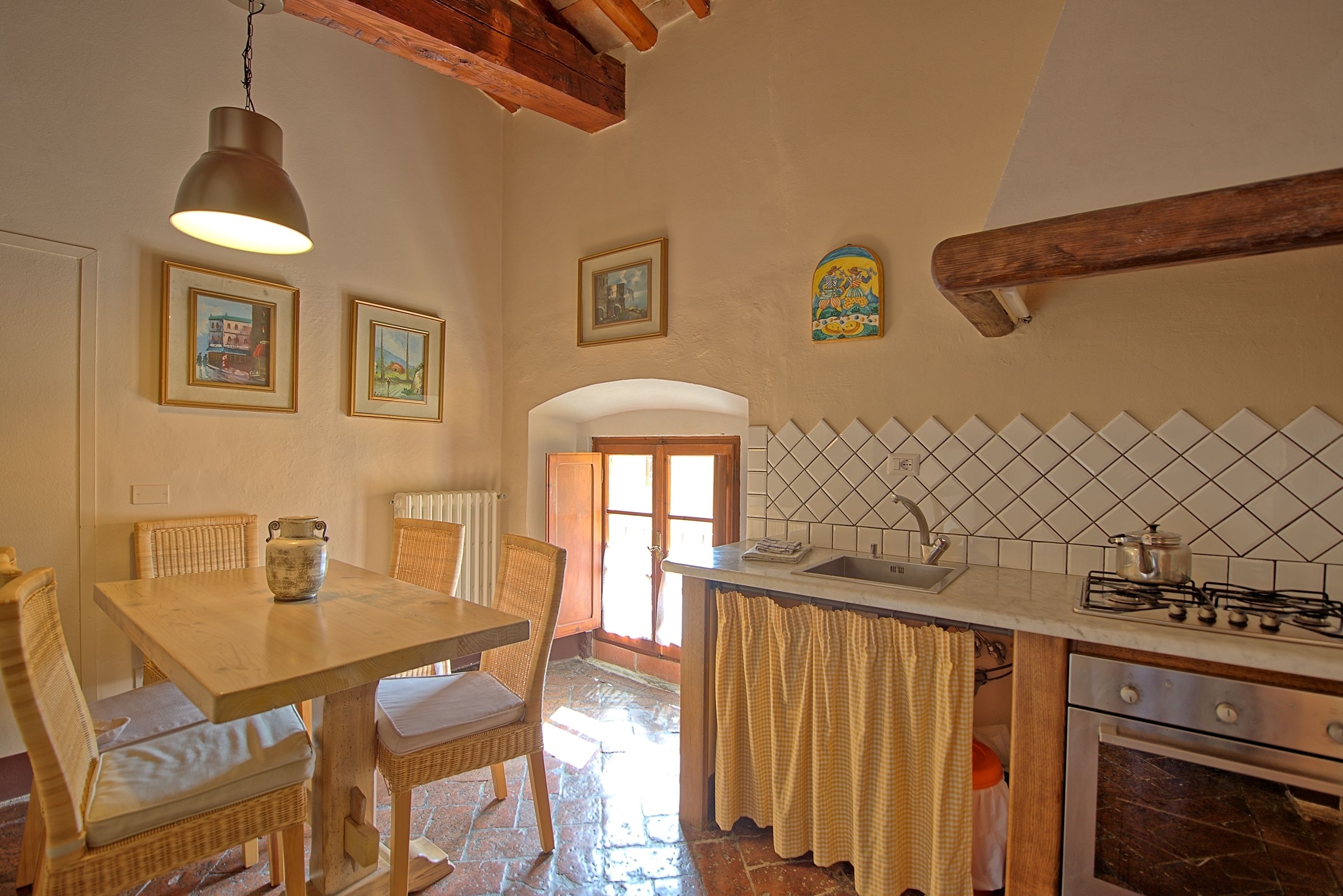 A kitchen with a wooden table, wicker chairs, a hanging light fixture, a tiled backsplash, and a stove.