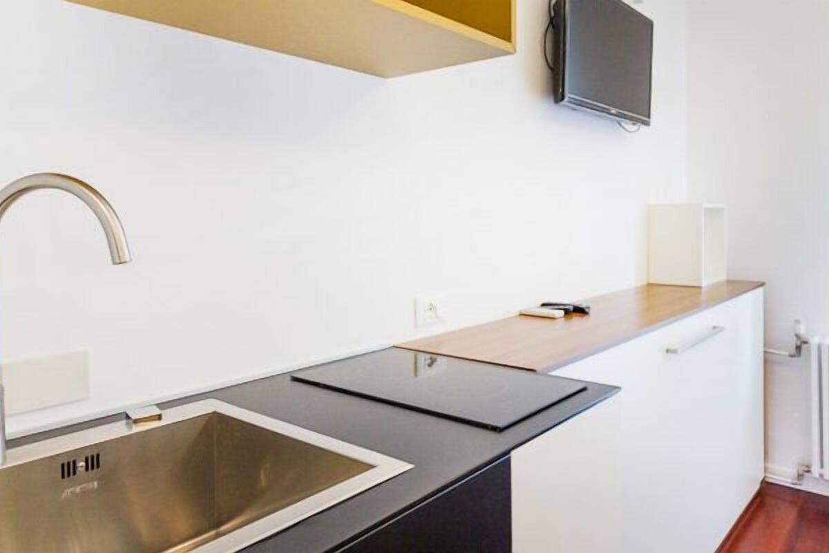 A modern kitchenette with a stainless steel sink, a flat-screen TV mounted above the counter, and a white radiator in the background.