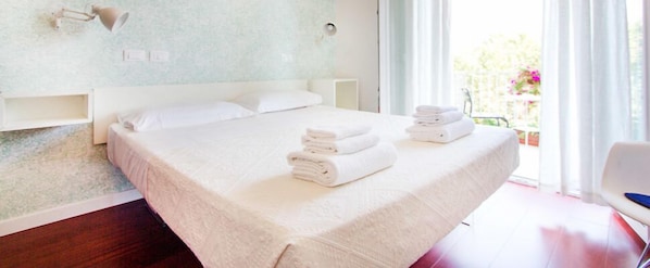 A hotel room with a large bed, white linens, a nightstand, and a view of a balcony with flowers. - Relais Star of Trastevere (Rome)