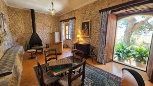 A rustic room with stone walls, a fireplace, a sofa, a dining table with chairs, and a view of greenery outside. - Asis de Marratxinet (Marratxi)