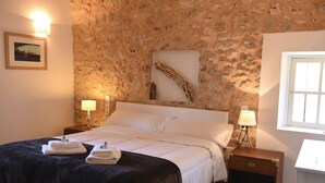 A bedroom with a stone wall, a bed with white linens, two bedside tables with lamps, and a framed picture on the wall. - Asis de Marratxinet (Marratxi)