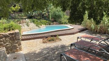 A swimming pool with a wooden deck, surrounded by greenery and stone walls.
