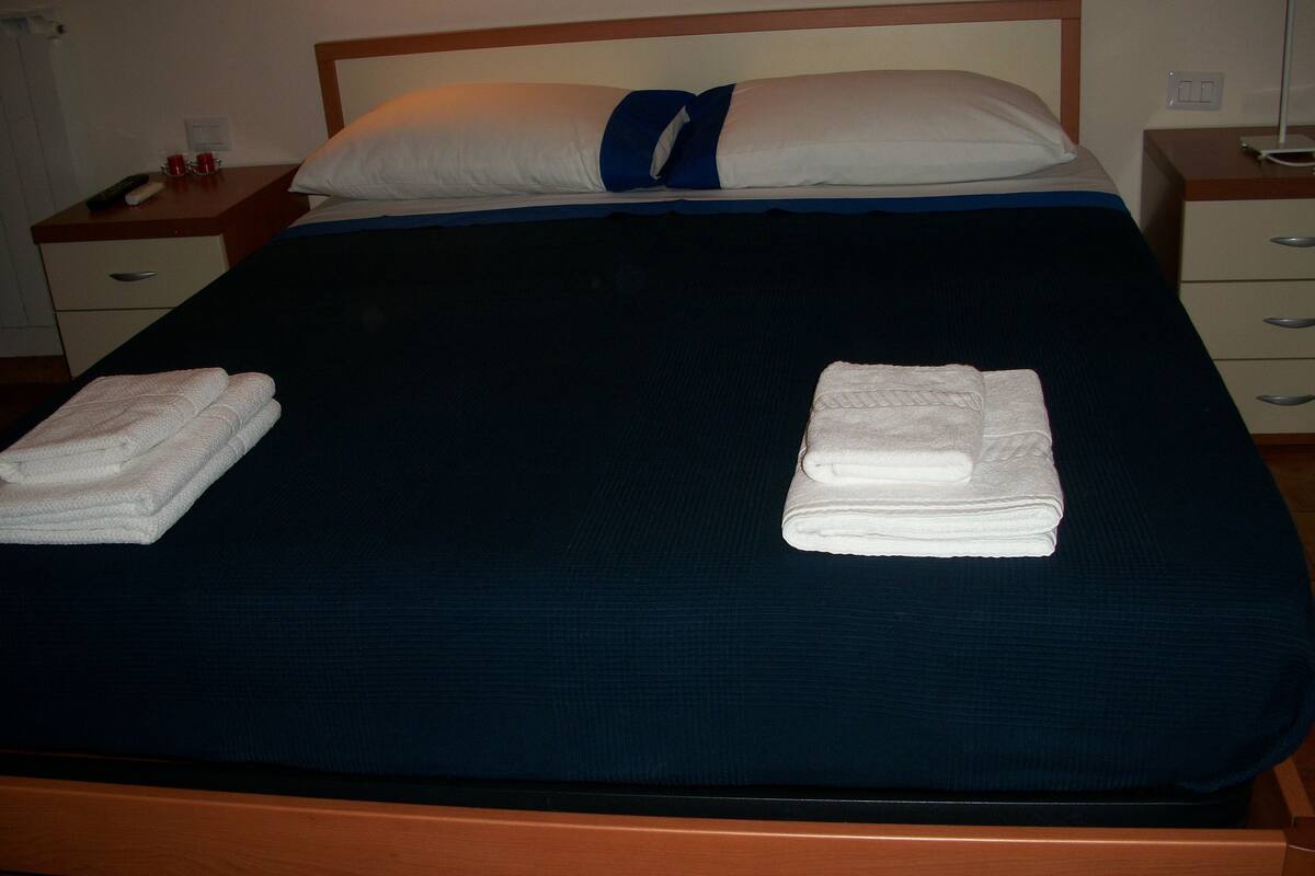 A neatly made bed with a dark blue bedspread, two folded white towels, and a pillow with a blue accent.