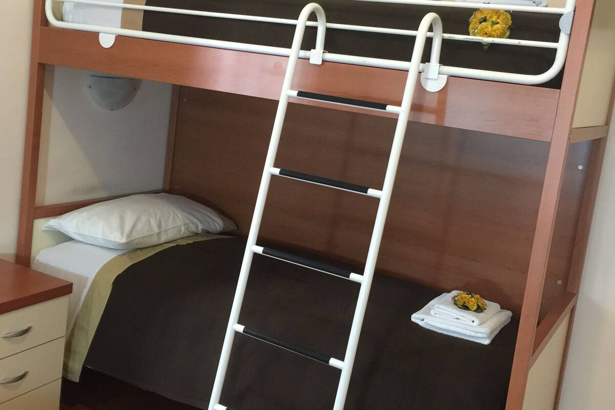 A bunk bed with a ladder, a bedside table, and a small shelf with towels.