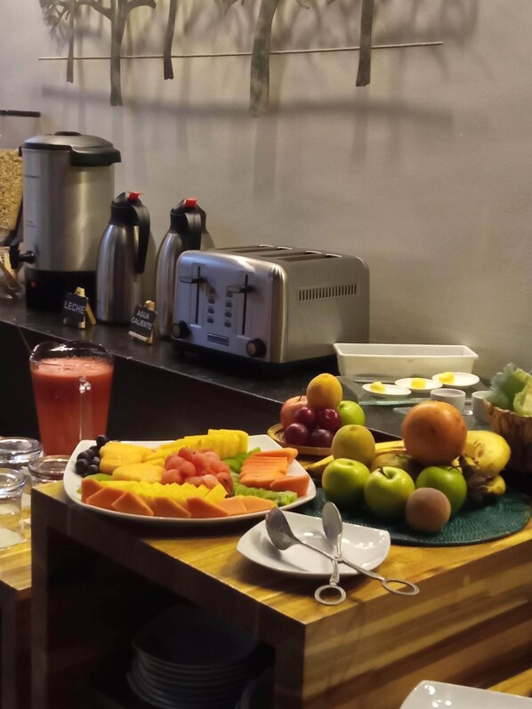 A breakfast setup with a toaster, a blender, and a variety of fruits and vegetables on a wooden table.