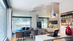 A modern living room with a sofa, chairs, a coffee table, and a TV. There is a bar area with bottles and a red vase. - GIO Hotel CITYFLATS Collection Bogotá (Bogotá)