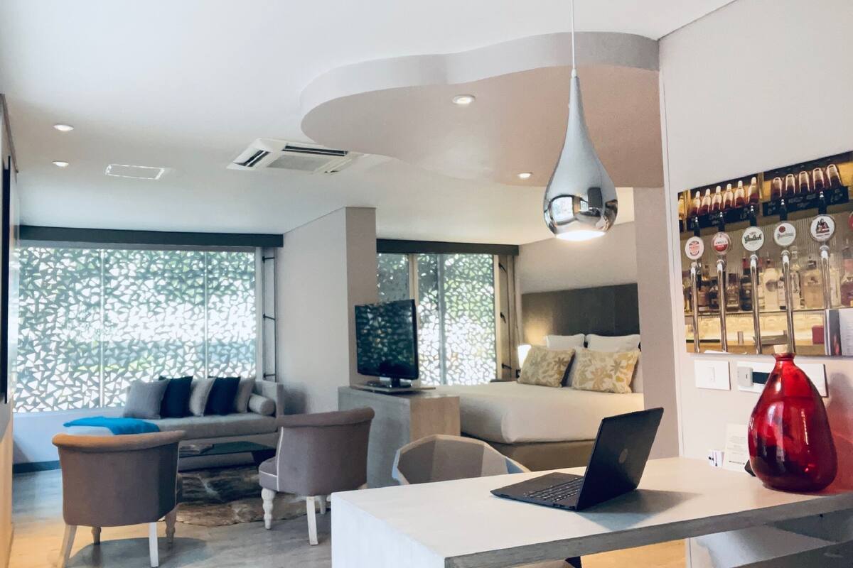 A modern living room with a sofa, chairs, a coffee table, and a TV. There is a bar area with bottles and a red vase.