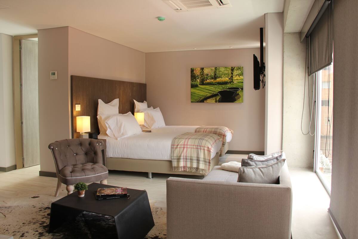 Une chambre d’hôtel avec un lit, une chaise, un canapé, une table basse et un tableau au mur.
