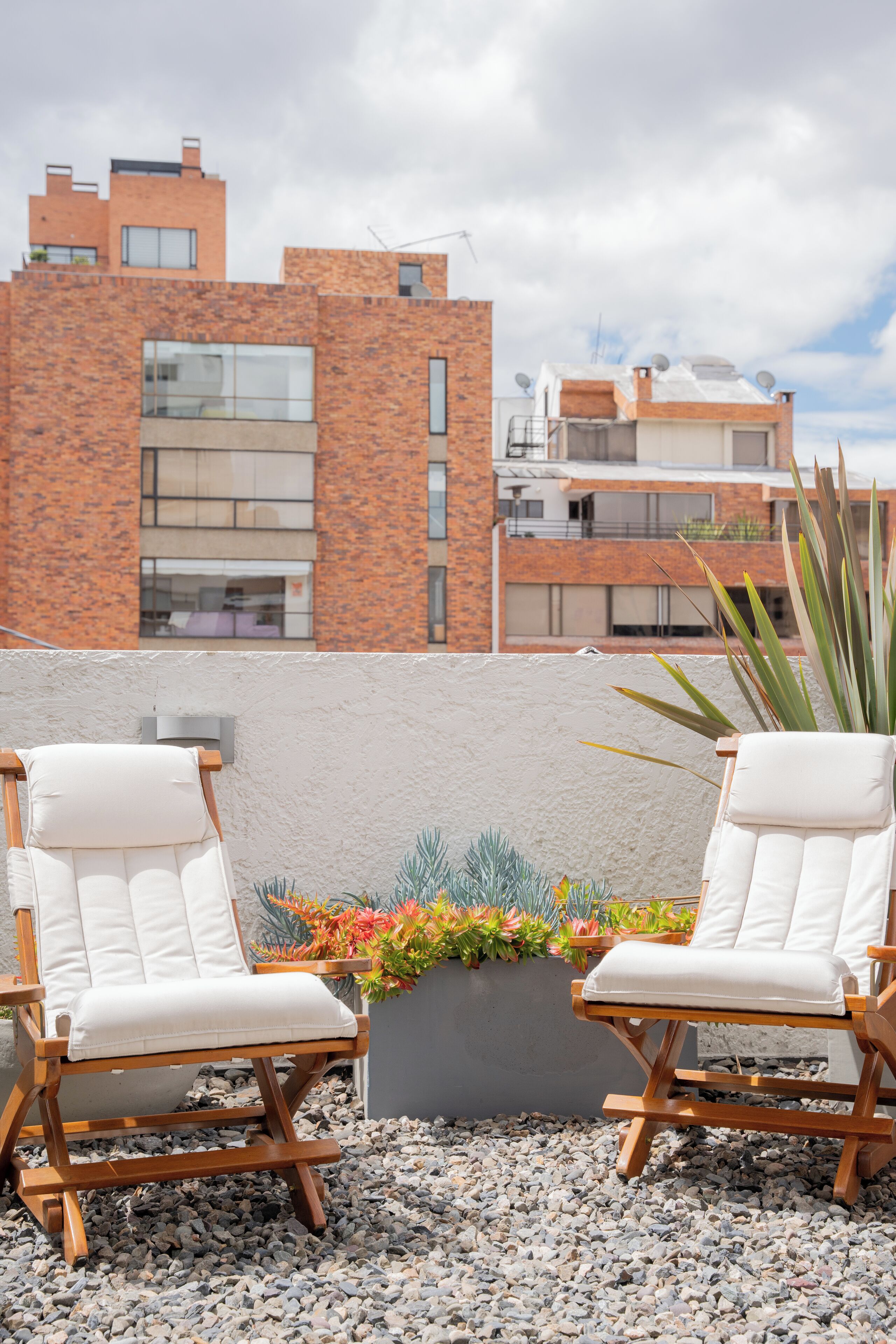 Two white cushioned chairs with wooden frames and a planter with colorful plants between them.