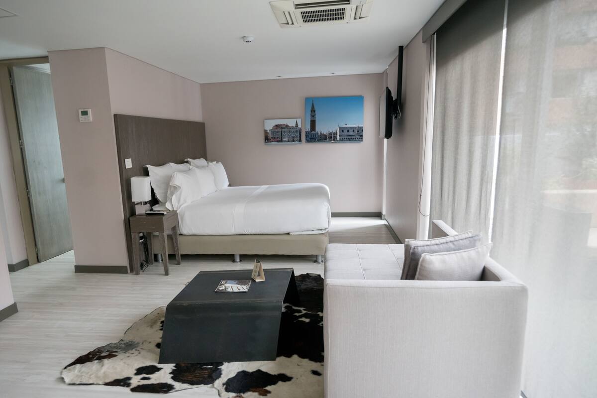 Une chambre d’hôtel moderne, dotée d’un grand lit, d’un canapé, d’une table basse et d’un téléviseur à écran plat fixé au mur.