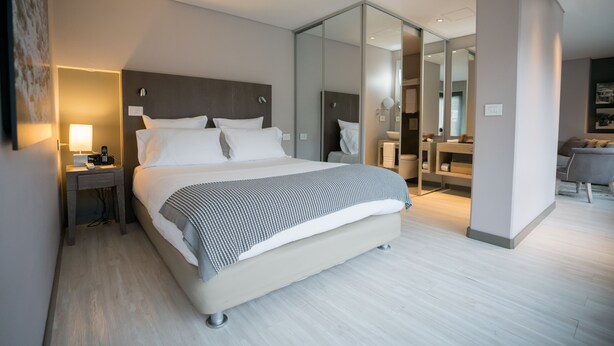 A modern hotel room with a large bed, bedside table with a lamp, and a mirror. - GIO Hotel CITYFLATS Collection Bogotá (Bogotá)
