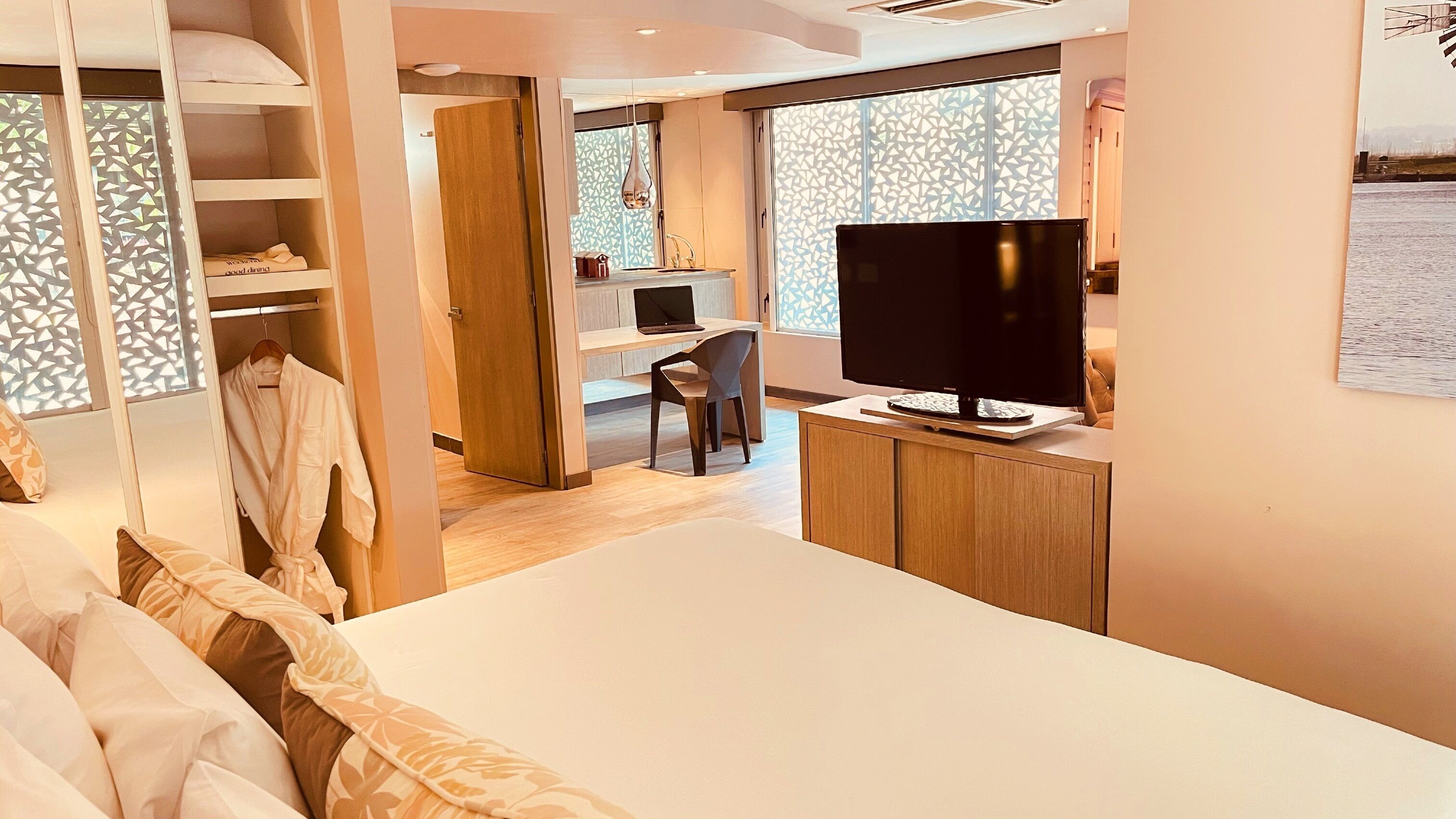 Quarto de hotel moderno com uma cama grande, uma escrivaninha com computador, televisão e guarda-roupa.