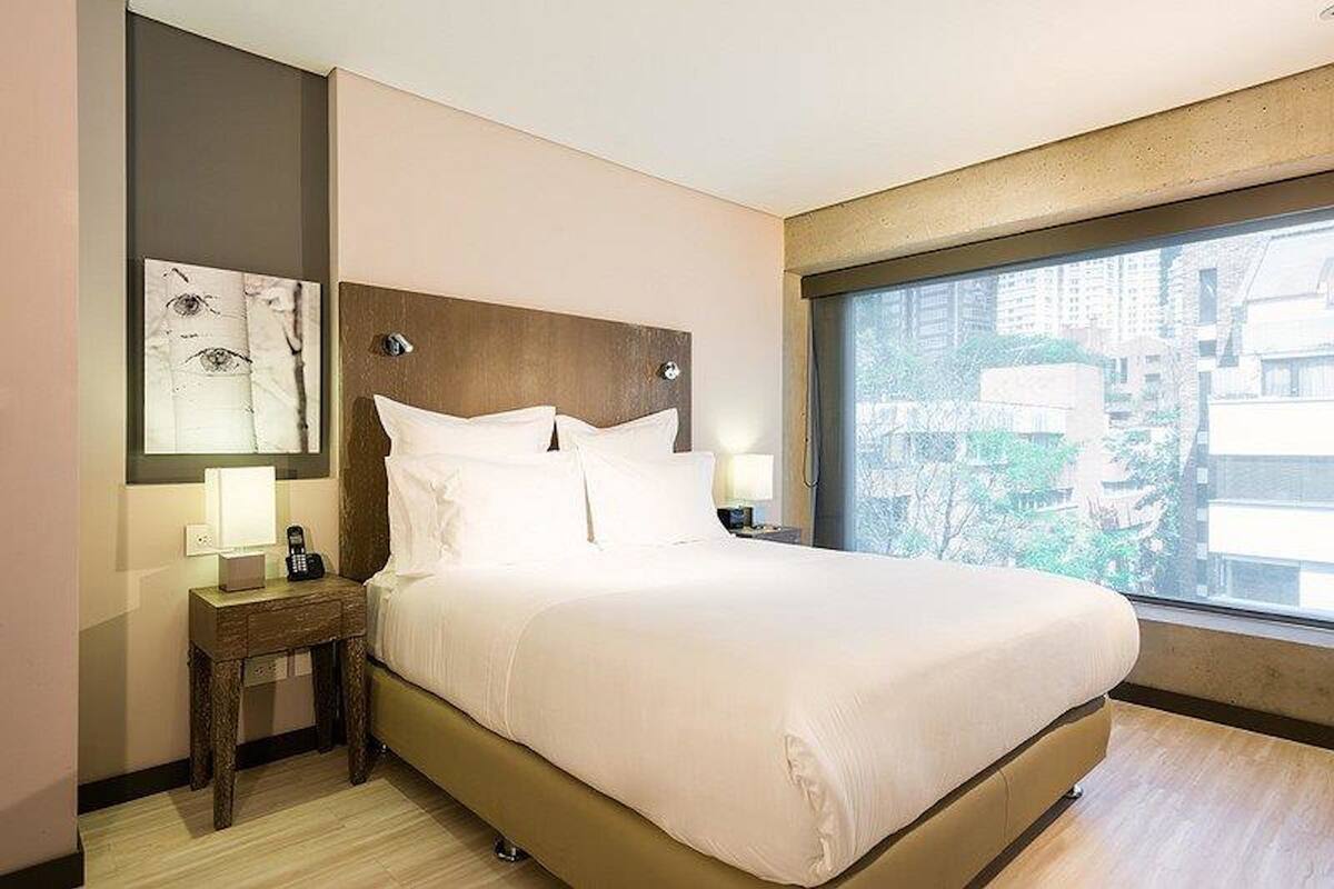 Une chambre d’hôtel avec un grand lit, une table de chevet avec une lampe et une vue sur la ville par une grande fenêtre.