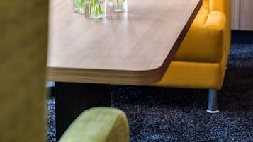 Een moderne woonkamer met een gele bank, een houten salontafel met vazen vol bloemen en een boekenkast met boeken en decoratieve objecten.