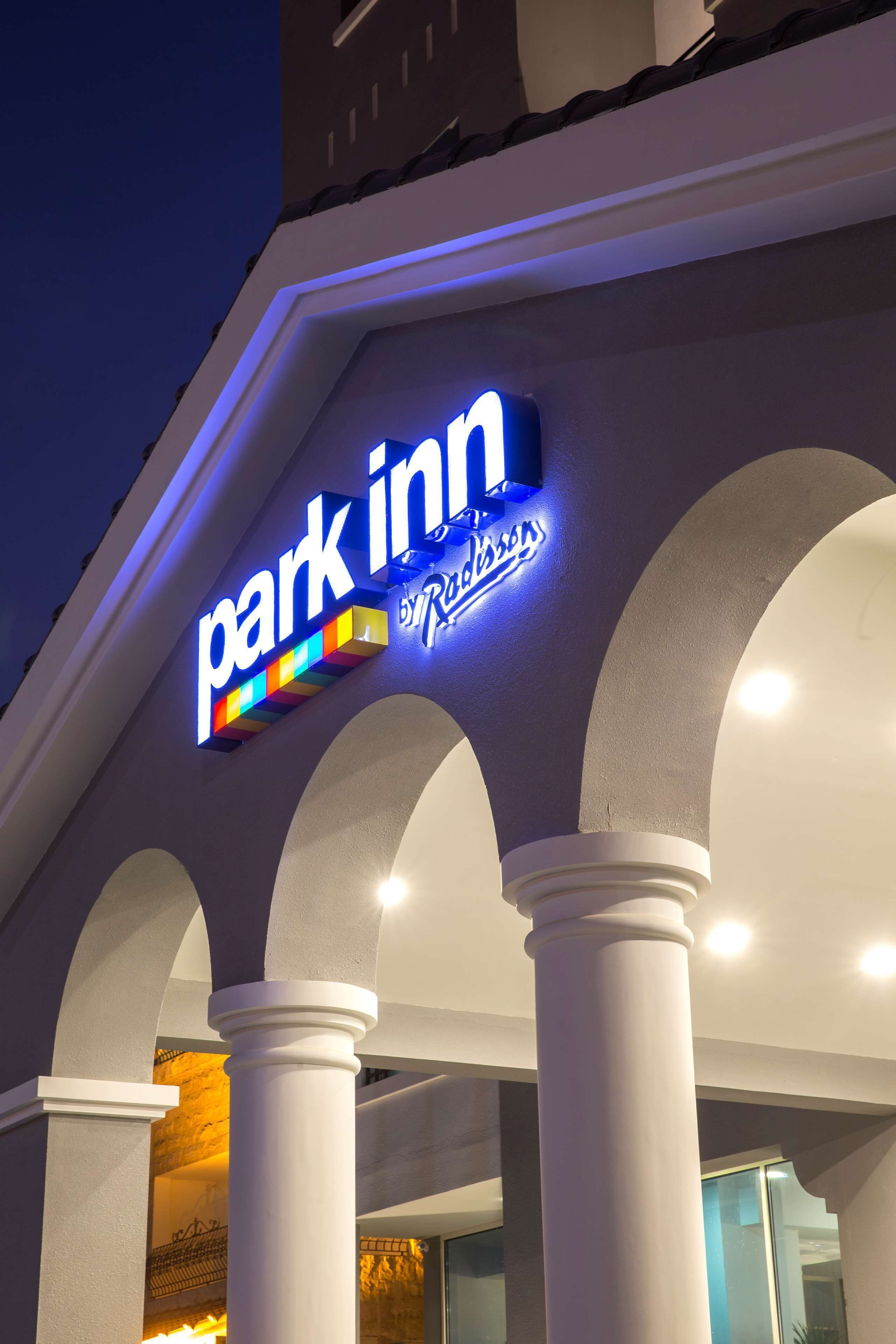 A hotel entrance with a 'Park Inn' sign, white columns, and a modern architectural design.