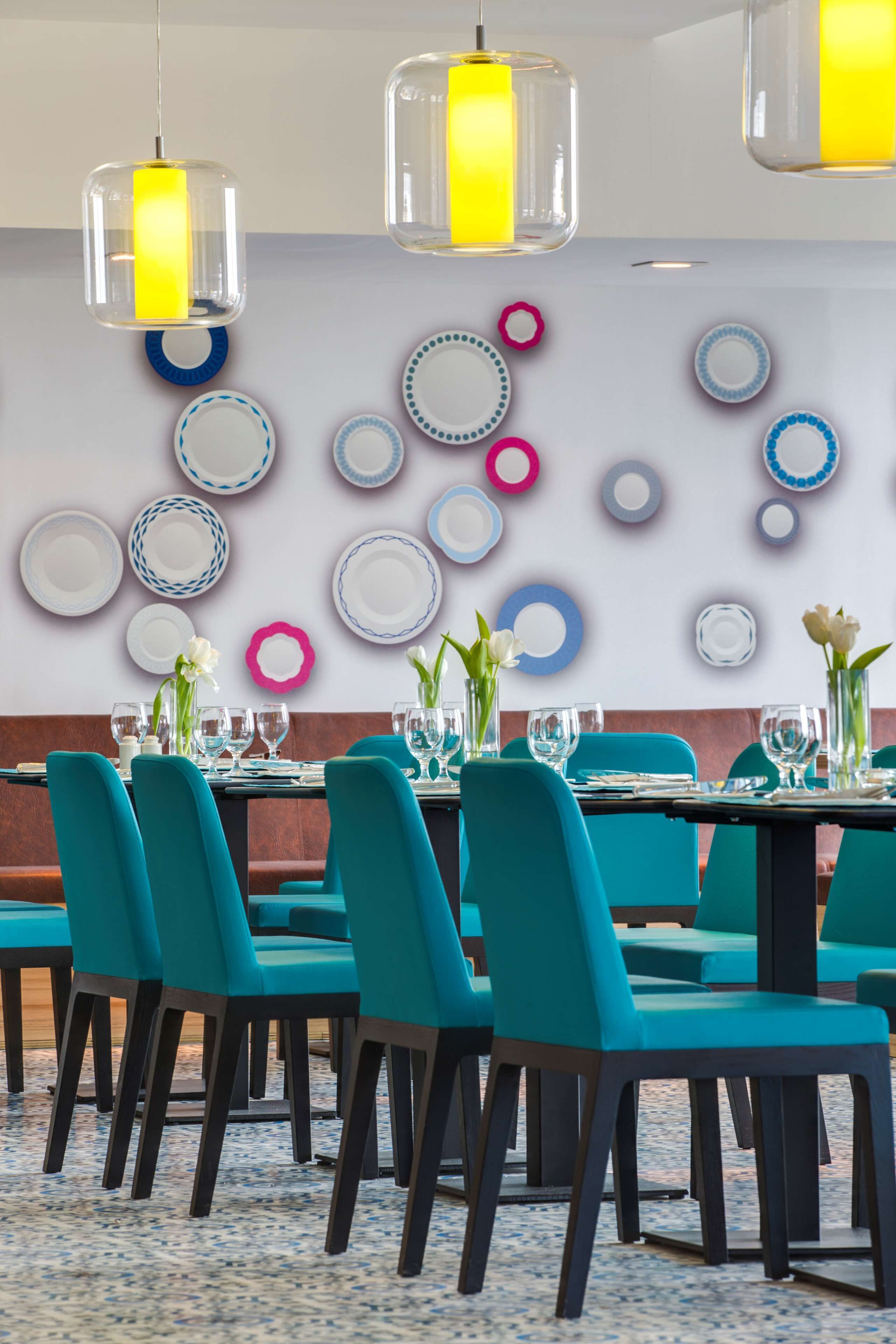 A dining area with teal chairs, a patterned floor, and a wall decorated with plates and vases.